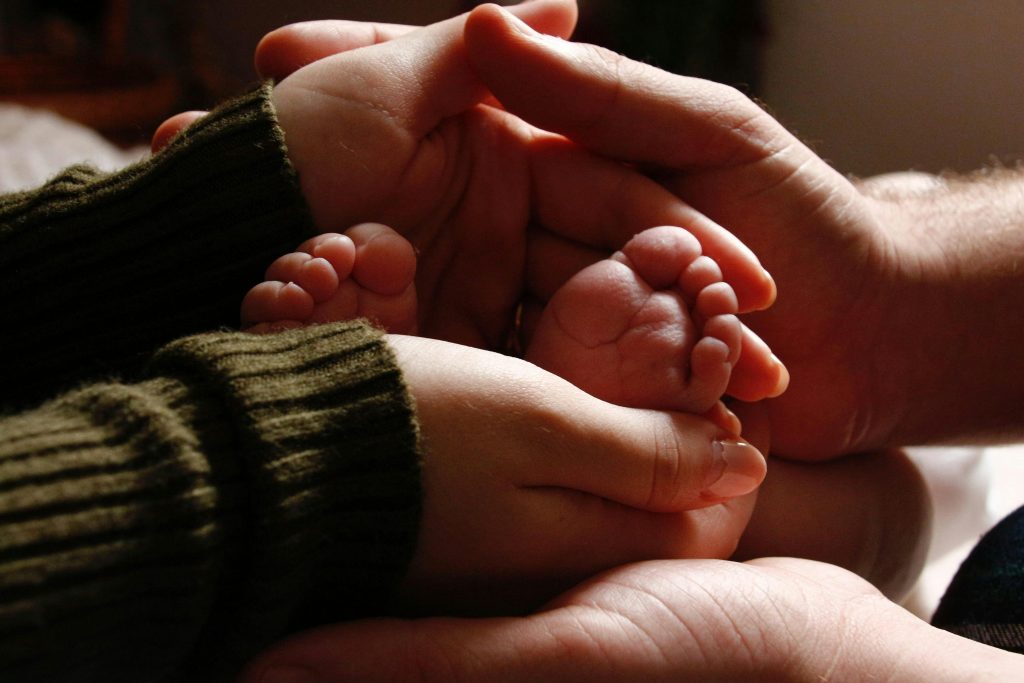 Manos de dos adultos sosteniendo los pies de un bebé — custodia compartida en España
